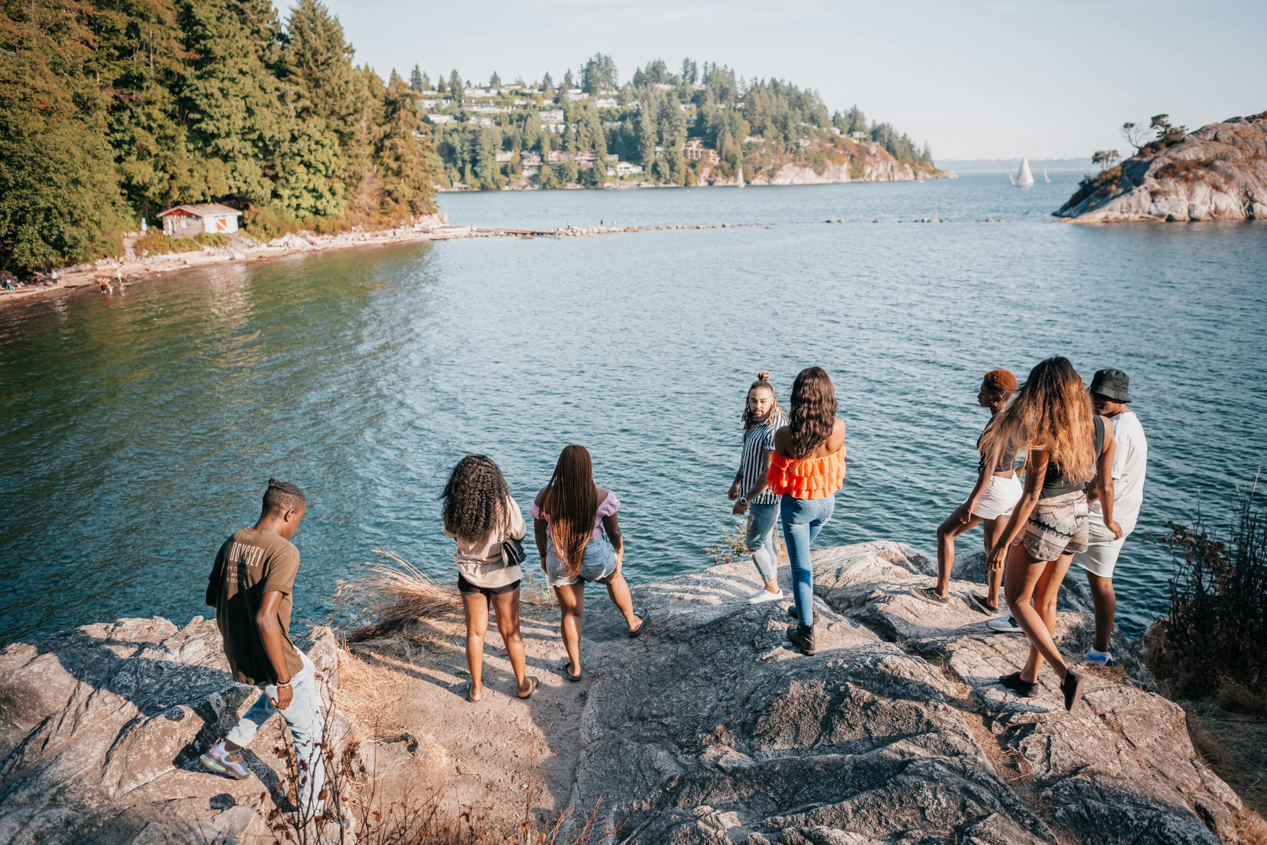 A diverse group of friends standing on rocks by a lake, surrounded by trees and water.